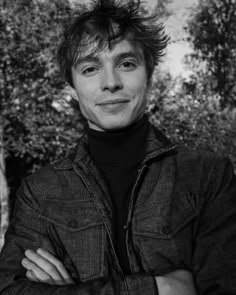 black and white photograph of a man with his arms crossed in front of some trees