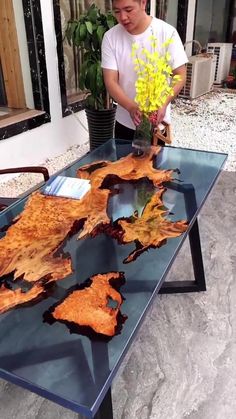 a man standing next to a table that has leaves on it and flowers in the vase