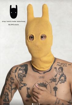 a man wearing a yellow bunny mask with tattoos on his chest and arm, standing in front of a white wall