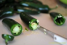 several green peppers cut in half on a cutting board with a knife next to them