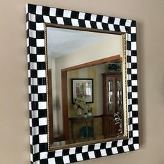 a black and white checkered mirror hanging on the wall next to a vase with flowers