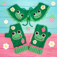 two green crocheted mittens with faces and flowers on them, sitting next to each other