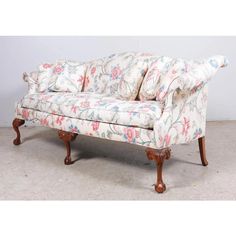 an old style couch with floral fabric on the back and arm rests against a white wall