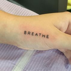 a person with a small tattoo on their left wrist that says breathe in black ink