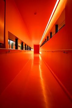 an empty hallway with bright orange walls and flooring is lit by red light at the end