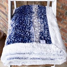 a white chair with a blue and white blanket on it's back, sitting in front of a brick wall