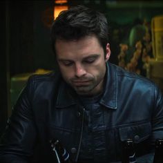 a man wearing a black leather jacket looking down at his cell phone while sitting in front of him