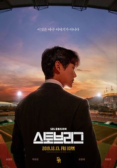 a man in a suit looking out over a baseball field at night with the sun setting behind him