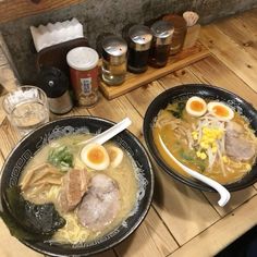 two black bowls filled with soup on top of a wooden table next to beer glasses