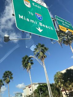 a green street sign sitting on the side of a road next to tall palm trees