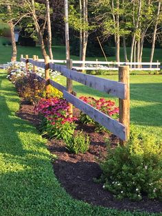 a wooden fence in the middle of a grassy area with flowers and trees around it