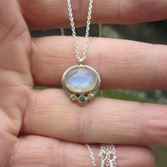 A smaller version of one of my best selling necklaces!! A gorgeous rainbow moonstone cabochon measuring 9 x 11mm is bezel set in a handmade 14k gold and sterling silver bezel setting. It's accented by a 3mm natural aquamarine** flush set in a hand made 14k gold nugget flanked by two plain gold nuggets. The design is understated... letting the gemstones be the focal point and giving the pendant a modern simplicity. The pendant is shown with a shiny/unoxidized finish in pics 1-3. Pic 4 shows the l Moonstone Gemstone Jewelry In Oval Cabochon, Unique Moonstone Round Pendant Jewelry, Sterling Silver Multi-stone Jewelry With Oval Cabochon, Celestial Moonstone Cabochon Jewelry, Sterling Silver Oval Cabochon Multi-stone Jewelry, Unique Blue Topaz Birthstone Jewelry, Moonstone Multi-stone Round Jewelry, Multi-stone Moonstone Round Jewelry, Moonstone Gemstone Oval Pendant Jewelry