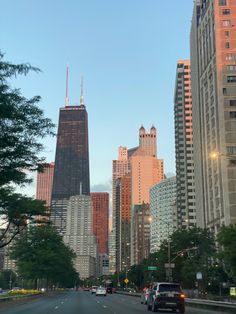 cars driving down the street in front of tall buildings with skyscrapers on either side