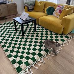 a cat walking across a living room floor next to a yellow couch and coffee table