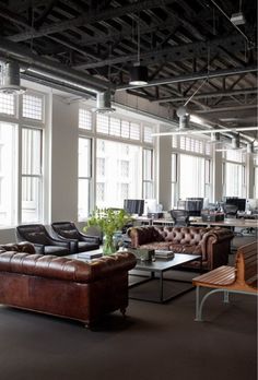 an office with couches, chairs and tables in the middle of the room that has large windows