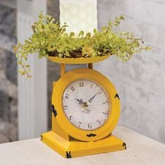 a yellow clock sitting on top of a table next to a planter filled with flowers