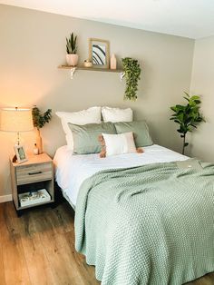 a bed sitting in a bedroom next to a nightstand with two plants on top of it