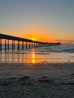 the sun is setting over the ocean with a long pier in the distance