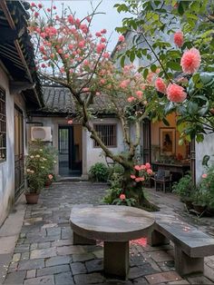 a stone bench sitting in the middle of a courtyard next to a tree with pink flowers on it