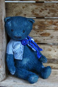 a blue teddy bear sitting on top of a wooden crate with a purple ribbon around it's neck