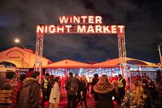 people are walking around in front of the winter night market sign at night with lights on