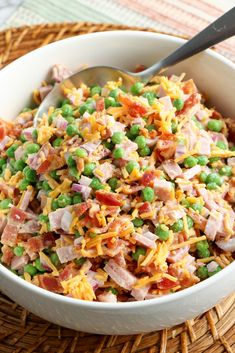 a bowl filled with peas and ham on top of a woven place mat next to a spoon