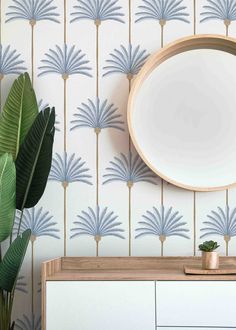 a round mirror sitting on top of a wooden cabinet next to a plant in a vase