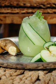 a glass filled with green liquid next to sliced apples and ginger on top of a plate