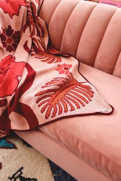 a pink couch with a red flowered blanket on it's back and side