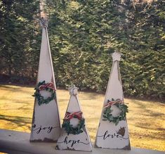 three wooden christmas trees are sitting on a ledge in front of some grass and trees