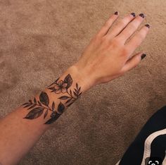 a woman's hand with a flower tattoo on her left wrist and black nails