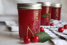 three jars filled with red liquid and cherries on top of a checkered table cloth