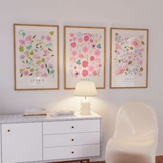 a white chair sitting next to a lamp on top of a wooden floor in front of two pictures