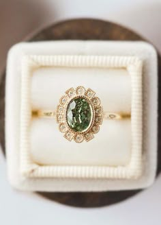 an engagement ring with a green stone sits in a white box on top of a table