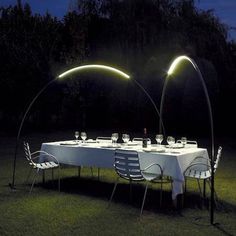 an outdoor dinner table set up in the dark with two lights shining on it's sides