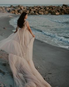 a woman in a long dress walking on the beach