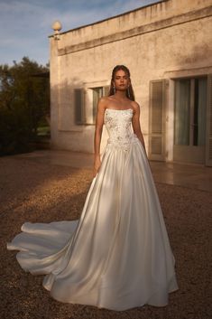 a woman in a white wedding dress standing on the ground near a building with shutters