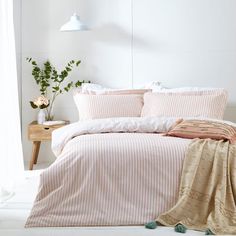 a bed with pink and white striped comforter next to a wooden table in front of a window