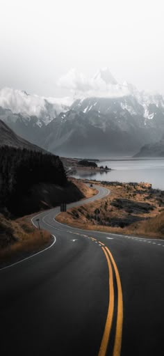 an empty road in the middle of nowhere with mountains in the background and snow on the tops