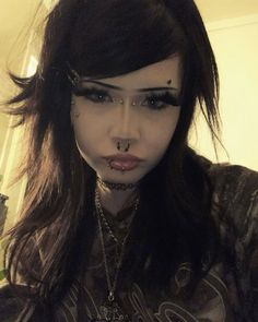 a woman with black makeup and piercings on her nose is looking at the camera