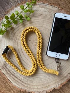 a cell phone on a yellow leash next to a tree stump with a plant in the background