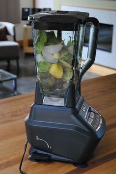 a blender filled with green vegetables on top of a wooden table