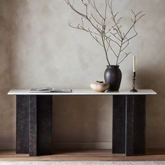 a table with a vase and some candles on it in front of a gray wall