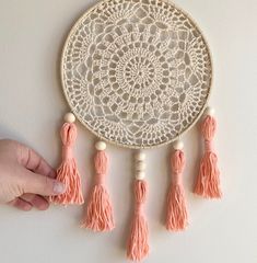 a hand is holding a doily with tassels on it and the wall hanging