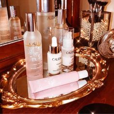 an assortment of beauty products sitting on a gold tray in front of a vanity mirror