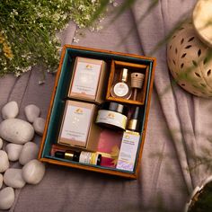 an open wooden box containing various items on a table with rocks and flowers in the background