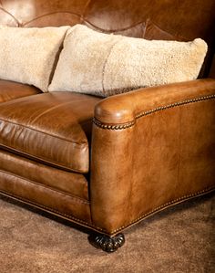 a brown leather couch with two white pillows on it's back and one beige pillow