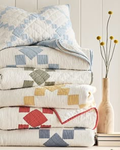 a stack of quilts and pillows sitting on top of a table next to a vase with flowers