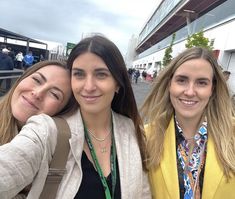 three women taking a selfie in front of a building with other people standing around