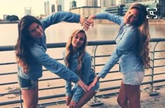 three young women are standing on the edge of a bridge and touching their hands together